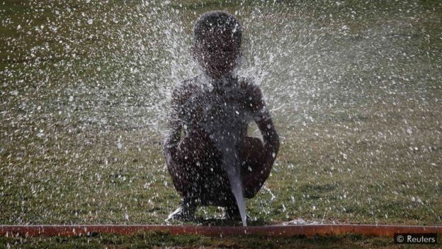 Niño refrescándose con una manguera.