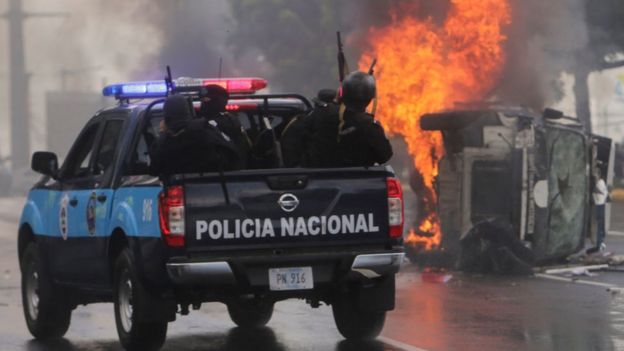 Una patrulla de la policía pasa frente a un auto quemado.