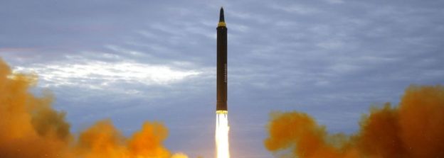 A missile is seen taking off from a grassy field in a burst of burning fuel and smoke