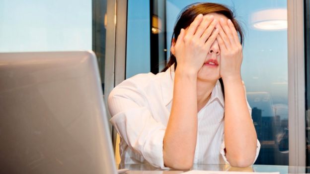 mujer usando computadora y tapándose la cara