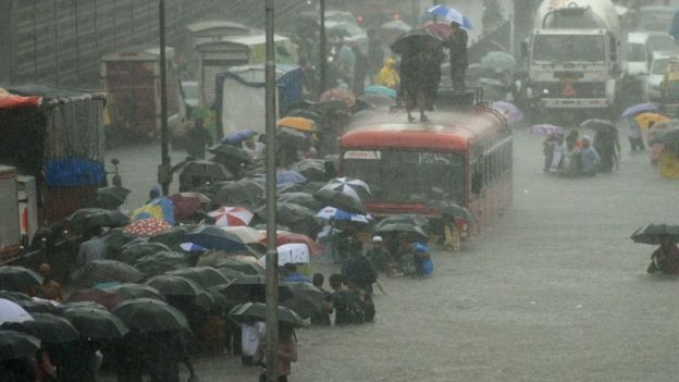 Residentes de la ciudad de Mumbai caminan en una calle inundada entre vehículos que no pueden avanzar por el agua.