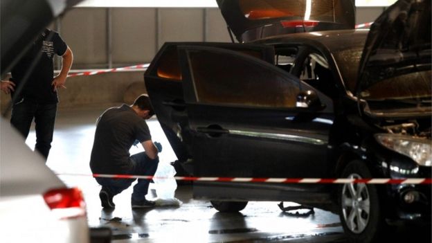 A forensic police officer crouches by a car abandoned by Redoine Faid at O'Parinor shopping mall car park