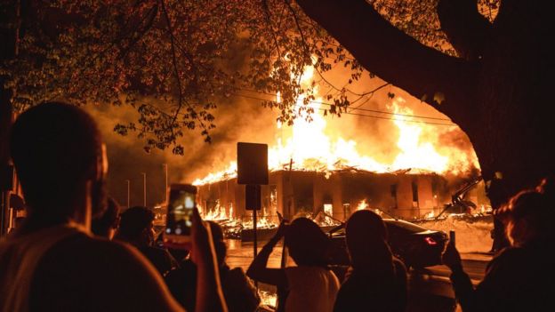 People look on as a construction site burns in a large fire near the Third Police Precinct