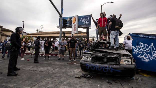 Protesters stand atop a burned out police car during protests over the Minneapolis arrest of George Floyd, who later died in police custody, in Los Angeles, California, 30 May 2020