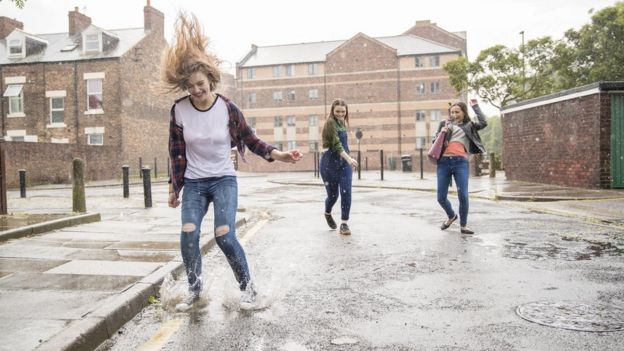 Meninas pulam e sorriem na rua sob chuva