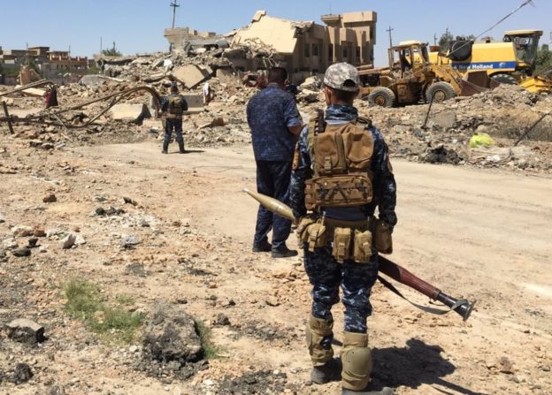 Armed men look out over a scene of destruction in Mosul