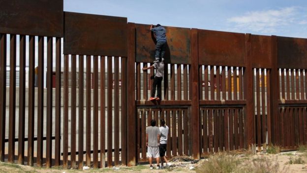 Una personas saltan el muro fronterizo entre Estados Unidos y México.