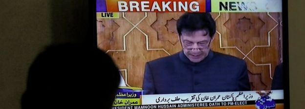 A man looks at a television screen displaying cricketer-turned-politician Imran Khan swearing in as Prime Minister of Pakistan