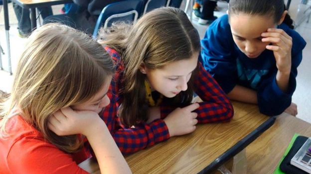 Meninas olham para tela de computador em sala de aula