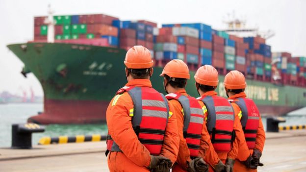 Workers wait to unload shipping containers on a port in Qingdao in China