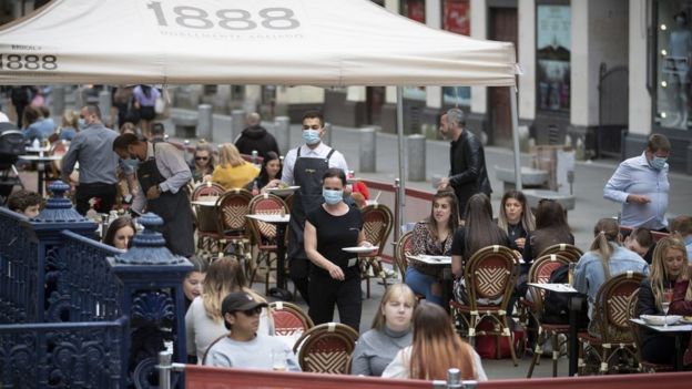 Staff at an outdoor restaurant wear masks as they serve food