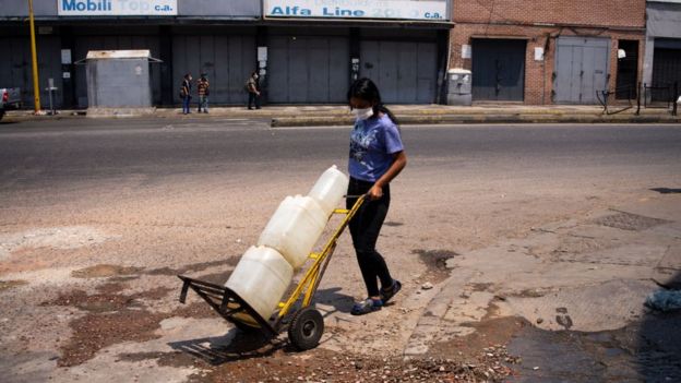 Una mujer traslada bidones de agua en Venezuela