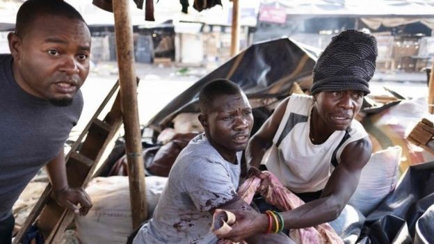 A wounded man reacts at the sight of soldiers while taking shelter in a stall at a market in Harare, on August 1, 2018