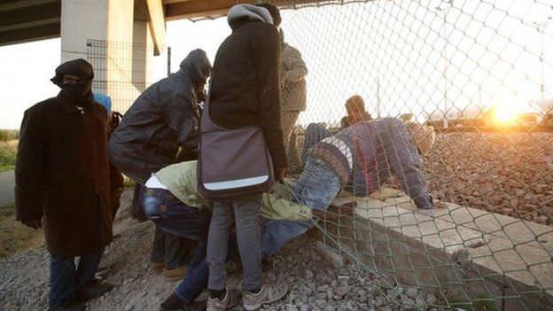 Migrants climb through a fence in Calais