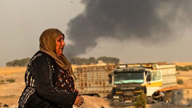 A woman walks as smoke billows following Turkish bombardment in Syria's town of Ras al-Ain