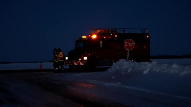 Still from video footage, darkened scene with snow and emergency vehicle visible