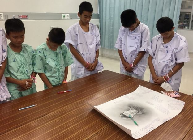 The young footballers bow their heads in commemoration after writing messages on a drawing of Samarn Gunan