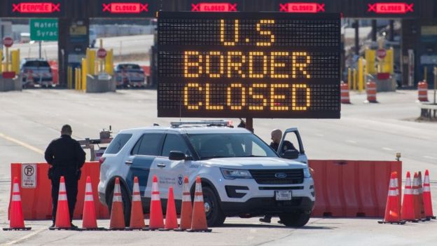 US Customs officers stand beside a sign saying that the US border is closed on March 22, 2020