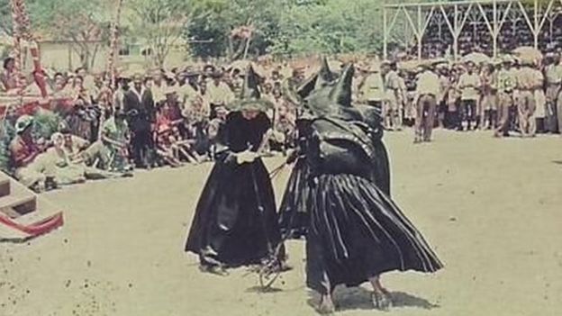 Three women dressed up as witches dance in this photograph from the 1958 Carnival in Antigua