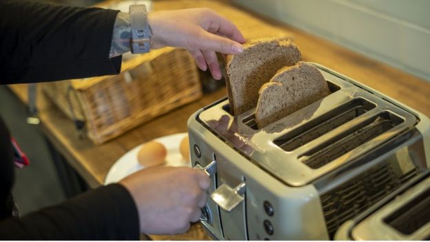 A woman places some bread in a toaster