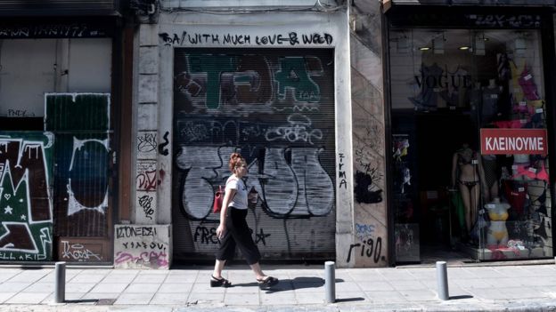 Mujer camina frente a la fachada de un almacén que lee "Cerramos" en la ciudad de Thessaloniki