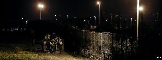 Migrants walk along the fence next to the railway to catch a train to reach England, in Calais, France, 30 July 2015