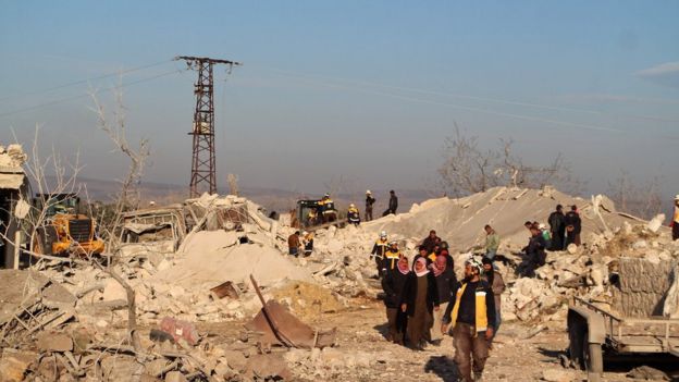 Rescuers and civilians walk through rubble