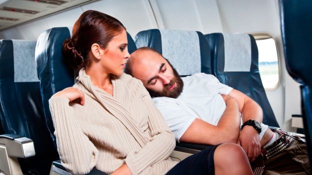 Un hombre se recarga en el hombro de una mujer en un avión