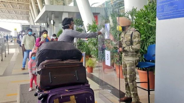 যাত্রীরা নিরাপত্তারক্ষীকে পরিচয়পত্র দেখাচ্ছেন কাঁচের শিল্ডের আড়াল থেকে