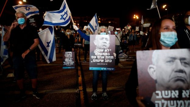 People hold up posters showing Benny Gantz and quoting him as saying: "I would not sit in a government under a man facing criminal indictment" at a protest in Tel Aviv on 19 April 2020