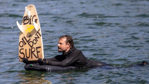 A protester in the harbour in Oslo, Norway holds up a surfboard with the political message: "Big Oil Don't Surf"