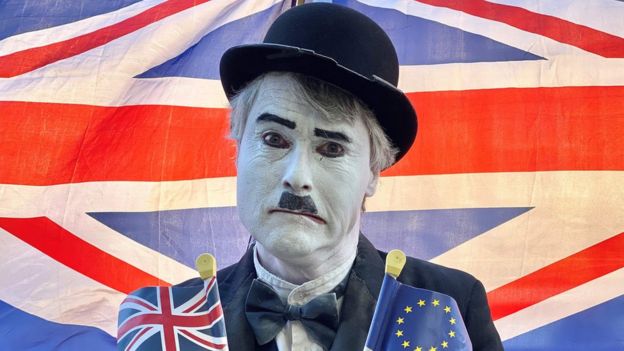Hombre maquillado como Charlie Chaplin con banderas de Reino Unido y la Unión Europea