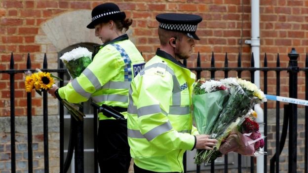 Police officers carry flowers left at the scene of multiple stabbings in Reading