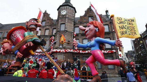 A carnival float in Dusseldorf shows a woman lighting a rocket with two men labelled "sexual offenders" tied to it.