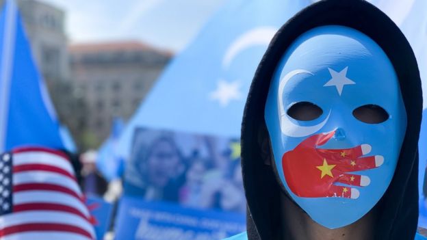 A demonstrator, wearing a mask with a Chinese flag on a hand over the mouth, protests in Washington