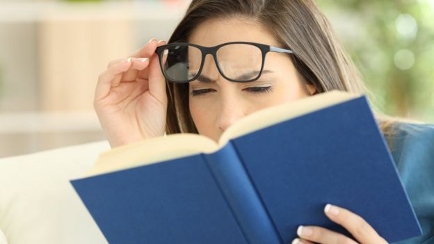 Mulher de óculos com dificuldade para ler livro