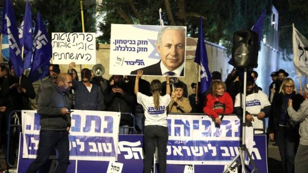 Supporters of Mr Netanyahu stand outside the prime minister's residence with signs