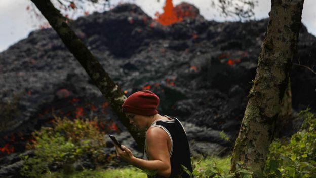 A man looks at his phone while walking in front of an eruption