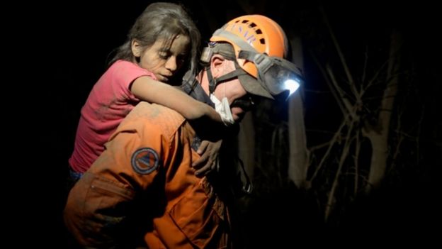 A rescue worker carries a child covered with ash after Fuego volcano erupted in El Rodeo, Guatemala, 3 June 2018