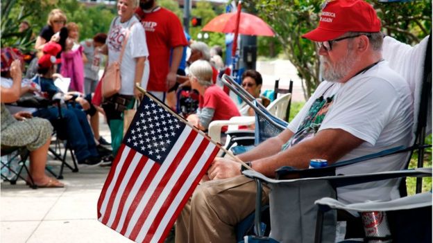 Supporters waiting outside arena holding flags, MAGA hats