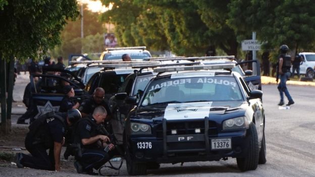 Mexican police take cover behind a car during a gun battle with cartel members