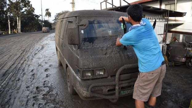 A resident cleans mud and ash from his car