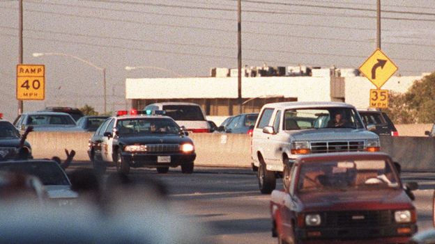 Motorists wave as police cars pursue the Ford Bronco (white, R) driven by Al Cowlings, carrying fugitive murder suspect O.J. Simpson, on a 90-minute slow-speed car chase June 17, 1994 on the 405 freeway in Los Angeles, California. Simpson's friend Cowlings eventually drove Simpson home, with Simpson ducked under the back passenger seat, to Brentwood where he surrendered after a stand-off with police.