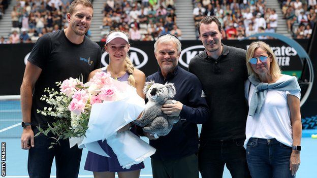 Caroline Wozniacki poses on court with her family after losing to Ons Jabeur at the Australian Open