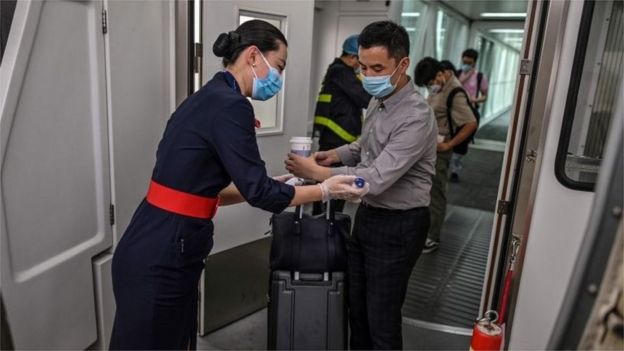 A flight attendant wearing a facemask (L) checks the body temperature of the passengers next to the door of the plane at the Tianhe Airport in Wuhan, in Chinas central Hubei province on May 29, 2020