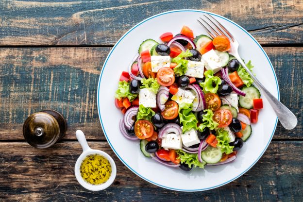 Una ensalada de queso, aceitunas, tomates y lechuga.