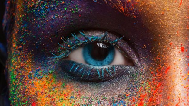 El ojo de una mujer y su cara pintada de diferentes colores.