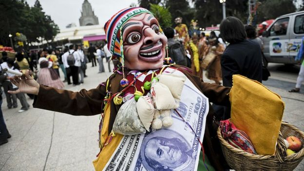 Hombre con una máscara baila. lleva al cuello un billete de 100 dólares gigante.