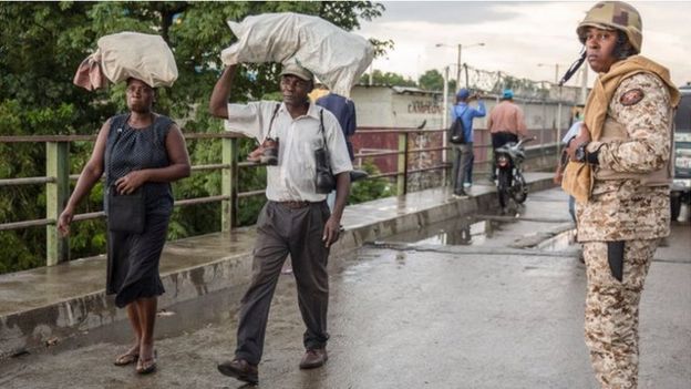 Oficial de la frontera, en puente, dos personas cruzan puente