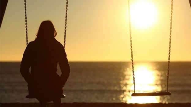 Person sitting on a swing with back to the camera looking into the distance as sun sets in the background